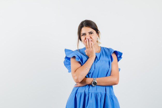 Jonge vrouw die hand op mond houdt in blauwe jurk en teleurgesteld kijkt