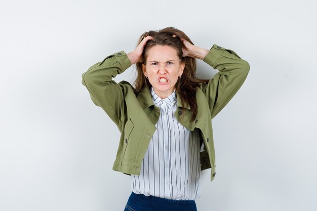 Jonge vrouw die handen op het hoofd houdt, haar tanden op elkaar klemt en er nerveus uitziet. vooraanzicht.