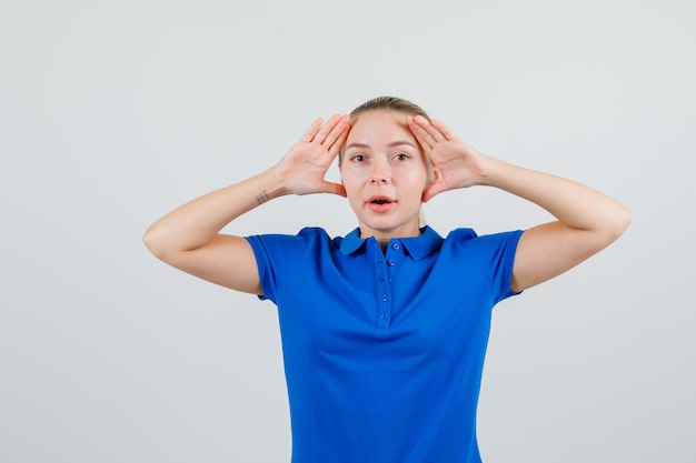 Jonge vrouw die handen opheft om duidelijk in blauw t-shirt te zien en nieuwsgierig kijkt