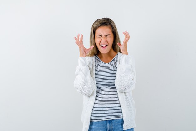 Jonge vrouw die handen opheft terwijl het schreeuwen in t-shirt, jasje en geïrriteerd, vooraanzicht kijkt.