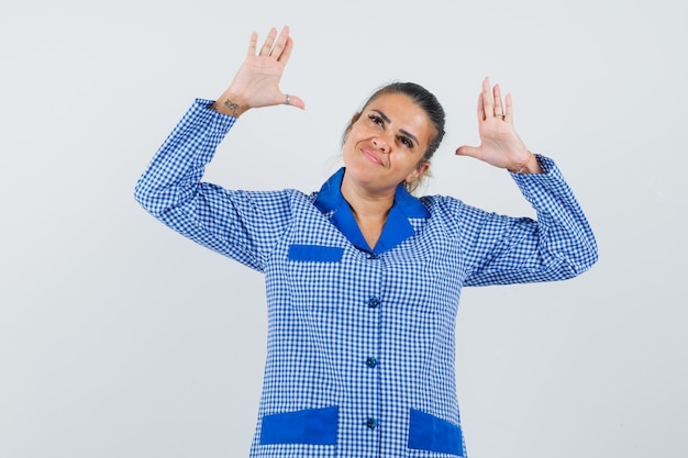 Jonge vrouw die handen opheft terwijl ze iets in het blauwe overhemd van de gingangpyjama probeert vast te houden en opgewonden kijkt. vooraanzicht.