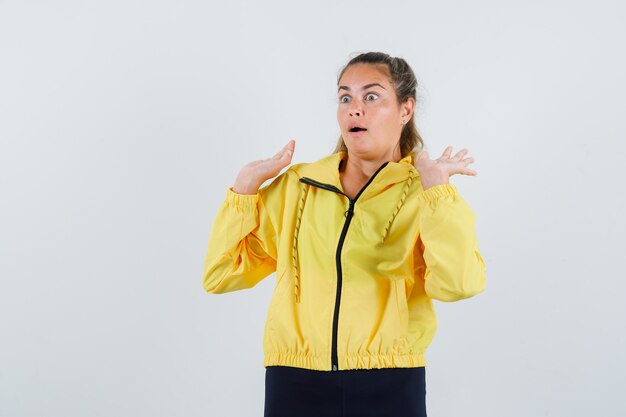 Jonge vrouw die handen opheft voor het verdedigen in gele regenjas en bang kijkt