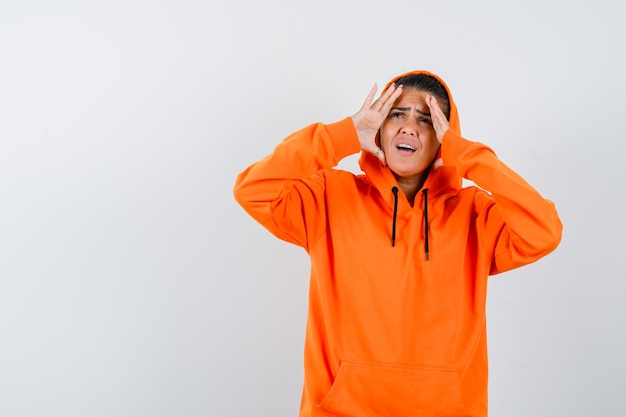 Jonge vrouw die handen vasthoudt in een oranje hoodie en er gefocust uitziet