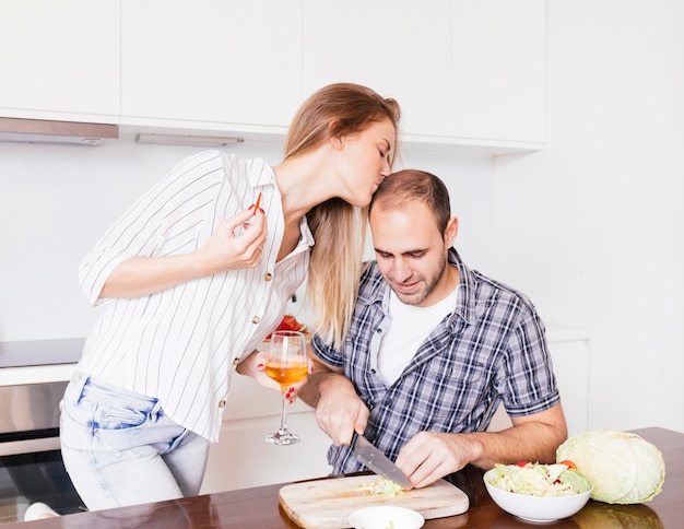 Jonge vrouw die het voorhoofd van haar echtgenoot kussen snijden de kool met mes