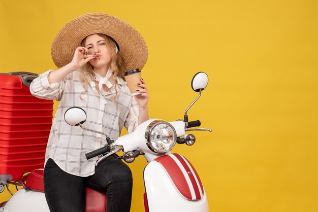 Jonge vrouw die hoed draagt en op motorfiets zit en koffie houdt die perfect gebaar maakt