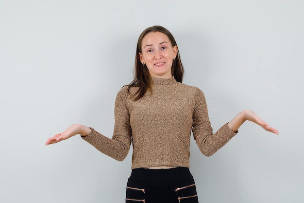 Jonge vrouw die hulpeloos gebaar in gouden blouse, vooraanzicht toont.