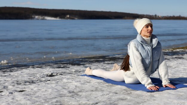 Jonge vrouw die in de winter op het strand buiten yoga beoefent