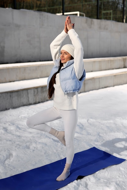 Gratis foto jonge vrouw die in de winter yoga buiten beoefent in warme kleren