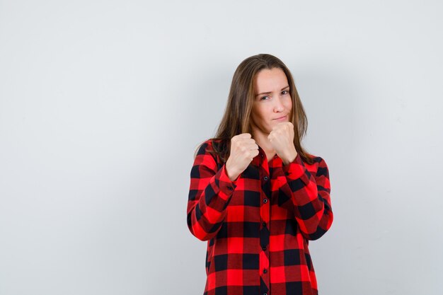 Jonge vrouw die in gevecht staat, poseert in een geruit overhemd en ziet er zelfverzekerd uit. vooraanzicht.