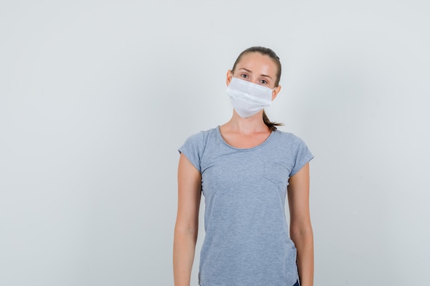 Jonge vrouw die in grijs t-shirt, masker, vooraanzicht kijkt.