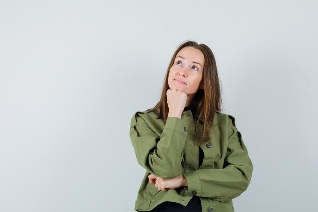 Jonge vrouw die in groen jasje droomt en peinzend, vooraanzicht kijkt.