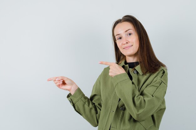 Jonge vrouw die in groen jasje opzij wijst en tevreden, vooraanzicht kijkt.