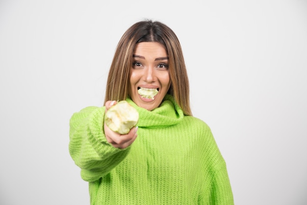 Jonge vrouw die in groene t-shirt een appel eet.