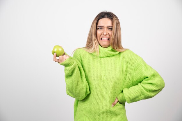 Jonge vrouw die in groene t-shirt een appel houdt.