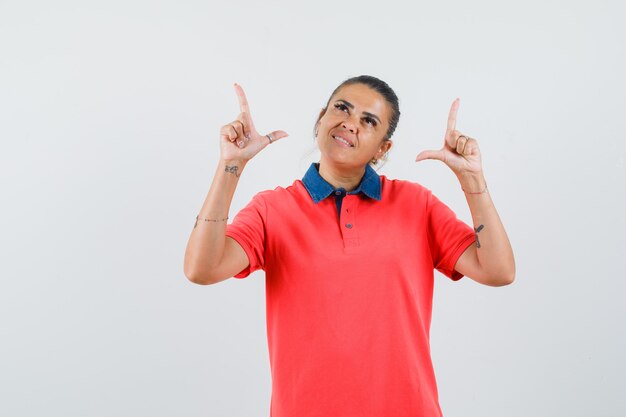 Jonge vrouw die in rood t-shirt benadrukt en mooi, vooraanzicht kijkt.