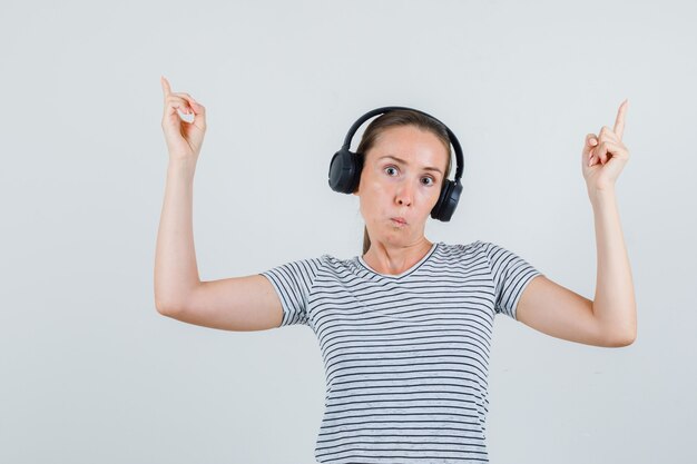 Jonge vrouw die in t-shirt, hoofdtelefoons benadrukt en verbaasd kijkt. vooraanzicht.