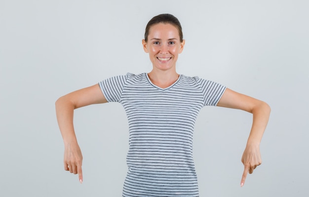 Gratis foto jonge vrouw die in t-shirt naar beneden wijst en gelukkig, vooraanzicht kijkt.