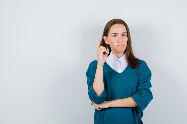 Jonge vrouw die in trui over wit overhemd wijst en er teleurgesteld uitziet. vooraanzicht.