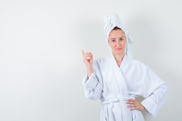 Jonge vrouw die in witte badjas, handdoek benadrukt en trots, vooraanzicht kijkt.