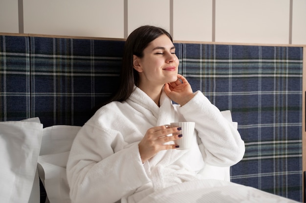 Gratis foto jonge vrouw die koffie drinkt terwijl ze op het bed in een hotelkamer zit