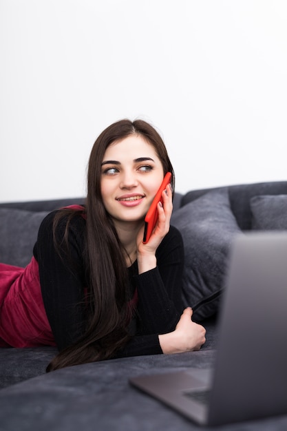 Jonge vrouw die laptop en cellphone op bank thuis gebruiken