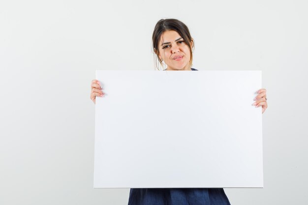 Jonge vrouw die leeg canvas in jurk vasthoudt en er zelfverzekerd uitziet