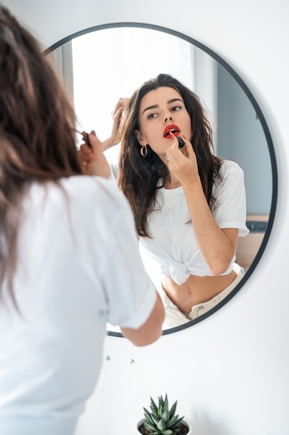 Jonge vrouw die lippenstift toepast die spiegel bekijkt