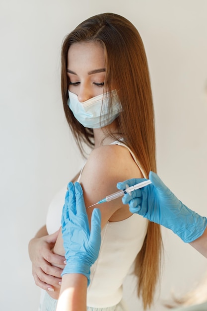 Gratis foto jonge vrouw die masker draagt en coronavirusvaccin ontvangt een jong meisje dat een immuniteitsschot in de onderarm krijgt close-up van arts in blauwe handschoenen die covid19 aids geeft