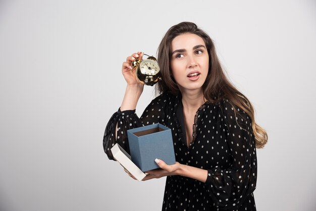 Jonge vrouw die met blauwe doos een wekker houdt