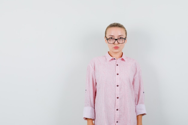 Jonge vrouw die met gevouwen lippen in roze overhemd, glazen kijkt