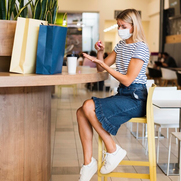 Jonge vrouw die met gezichtsmasker handen desinfecteert