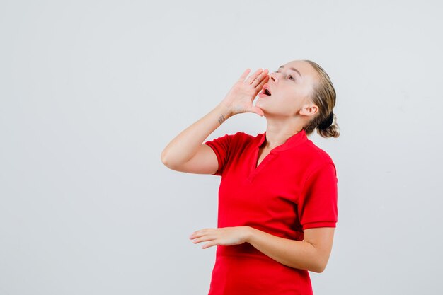 Jonge vrouw die met hand dichtbij mond in rood t-shirt schreeuwt