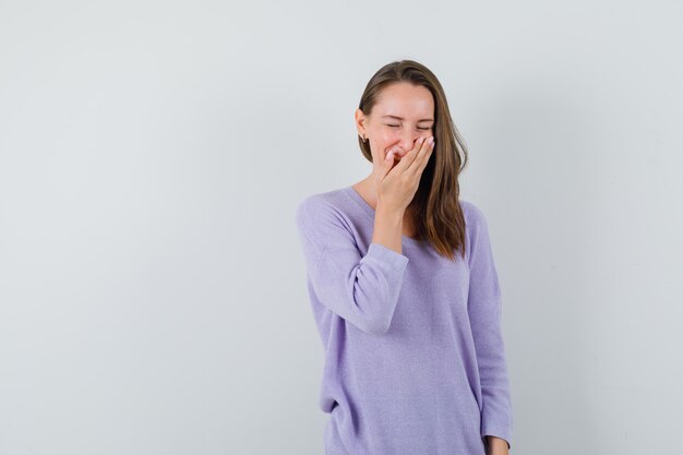 Jonge vrouw die met hand op mond in lila blouse lacht en vrolijk kijkt