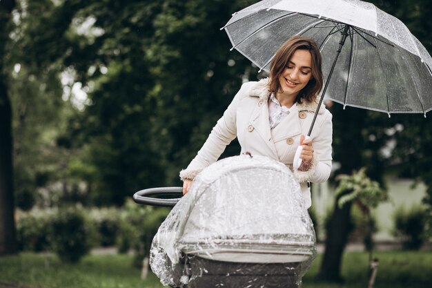 Jonge vrouw die met kinderwagen onder de paraplu in een slecht weer lopen