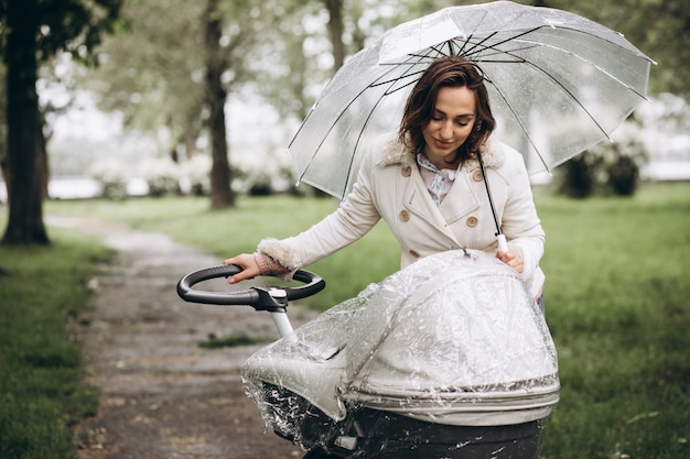 Jonge vrouw die met kinderwagen onder de paraplu in een slecht weer lopen