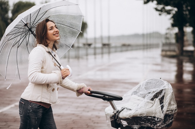 Jonge vrouw die met kinderwagen onder de paraplu in een slecht weer lopen