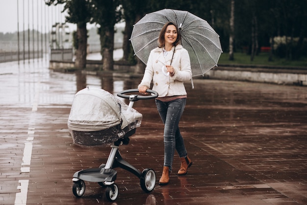 Jonge vrouw die met kinderwagen onder de paraplu in een slecht weer lopen