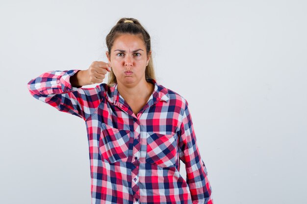 Jonge vrouw die met vuist in casual overhemd dreigt en hatelijk kijkt. vooraanzicht.