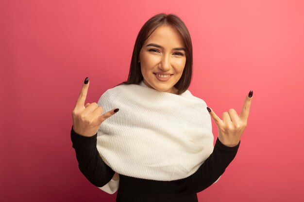 Jonge vrouw die met witte sjaal vrolijk het tonen van rotssymbool glimlachen