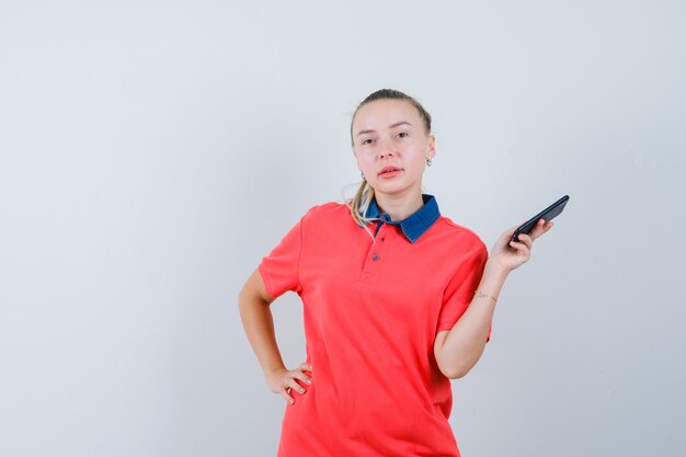 Jonge vrouw die mobiele telefoon in t-shirt houdt en zelfverzekerd kijkt