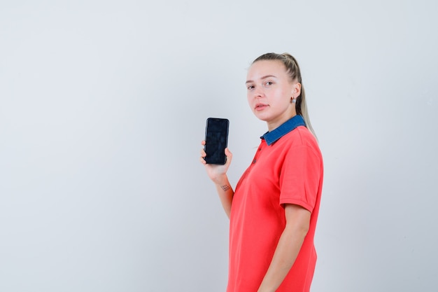 Jonge vrouw die mobiele telefoon in t-shirt houdt en zelfverzekerd kijkt