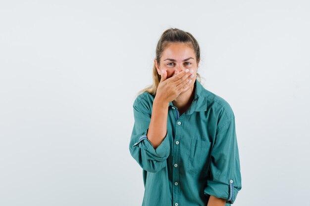 Jonge vrouw die mond behandelt met hand terwijl lachend in groene blouse en schattig kijkt