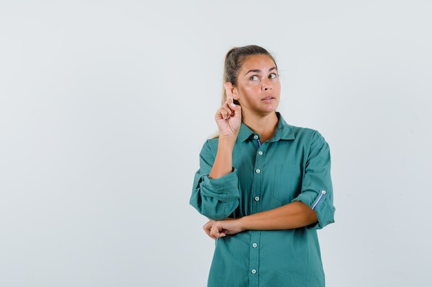 Jonge vrouw die nieuw ideegebaar in blauw overhemd toont en peinzend kijkt