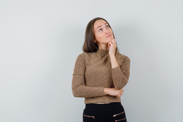 Jonge vrouw die omhoog in gouden blouse kijkt