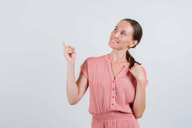 Jonge vrouw die omhoog met vinger omhoog in gestreepte kleding kijkt en vrolijk, vooraanzicht kijkt.