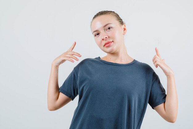 Jonge vrouw die omhoog wijst en in grijs t-shirt glimlacht