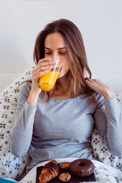 Jonge vrouw die ontbijt in bed heeft