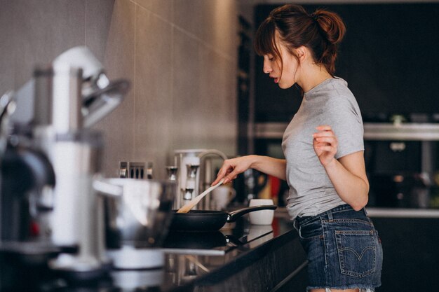 Jonge vrouw die ontbijt in keuken in de ochtend voorbereidt