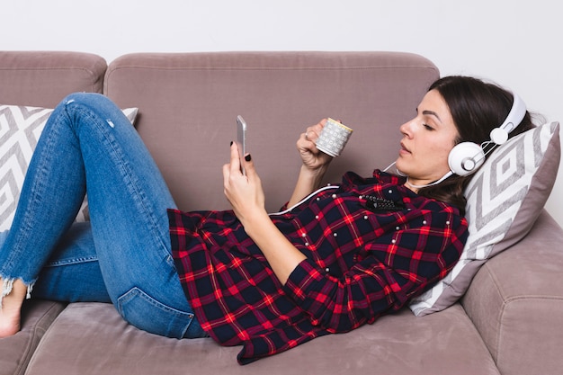 Gratis foto jonge vrouw die op bank het luisteren muziek op hoofdtelefoon ligt