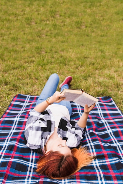 Gratis foto jonge vrouw die op deken over het groene boek van de graslezing ligt